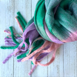 Colourful cosy thick scarf with tassels on a light white wooden surface, greens and pinks, pastel colours